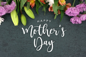Spring season still life with Happy Easter greeting holiday script over dark blackboard background texture with beautiful colorful white, pink, orange, purple and green flower blossom bouquet on top