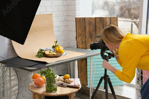 Young woman taking picture of lemons, mint and ginger in professional studio. Food photography