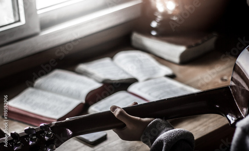 Young man is playing guitar and sing a song from Christian hymn book at home photo