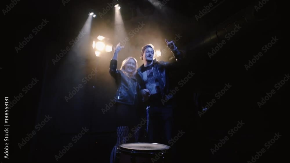 couple in rock-n-roll style, young couple on scene in spotlight kissing at dark background and expression makes the rock n roll gesture couple in rock-n-roll style, young couple on scene in spotlight kissing at dark background and expression makes the rock n roll gesture