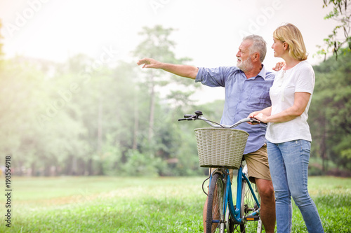 Senior old men couple walking their bike along happily talking happily.