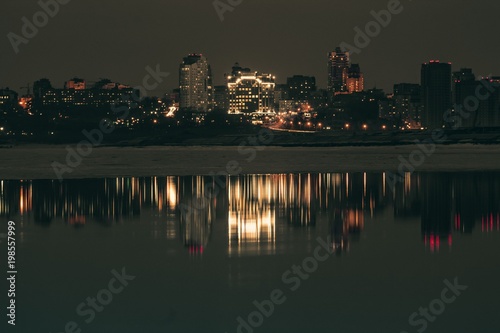Night city view with lots of lights and its reflection in a river water