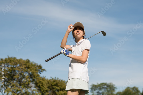 Female Asian golfers stood in the hot sun with golf clubs.