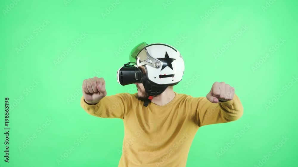 One young trendy guy in wearable emulator spectacles equipment playing game standing in chromakey greenbox close up isolated. Male person in vr-glasses enjoyment alone, motorcyclist rider at motor One young trendy guy in wearable emulator spectacles equipment playing game standing in chromakey greenbox close up isolated. Male person in vr-glasses enjoyment alone, motorcyclist rider at motor