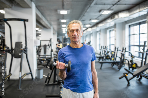 Confident senior man holding dumbbell in gym