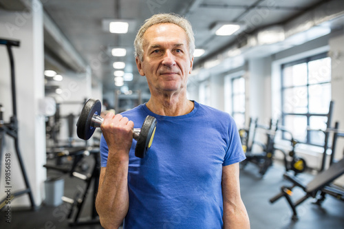 Strong senior man holding dumbbell in gym