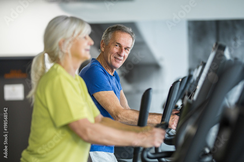 Happy senior couple training on stair stepper at gym