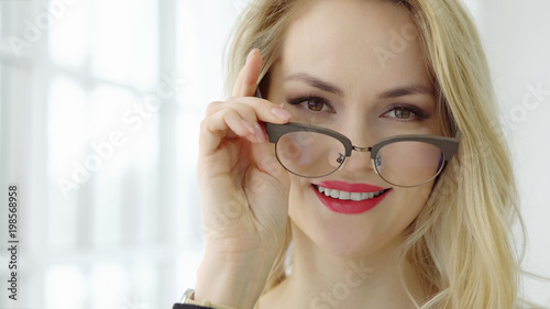 Close up of a young beautiful woman with glasses at the window and looking at camera.