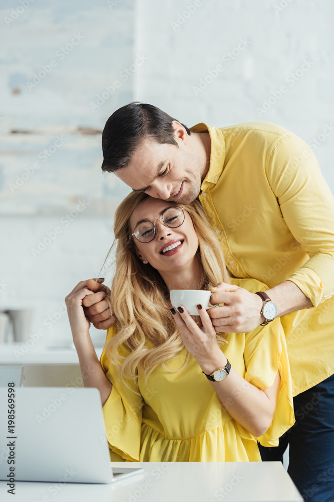 Smiling man giving coffee to woman working by laptop Smiling man giving coffee to woman working by laptop