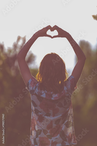 Girl holding a heart-shape with hands in nature.