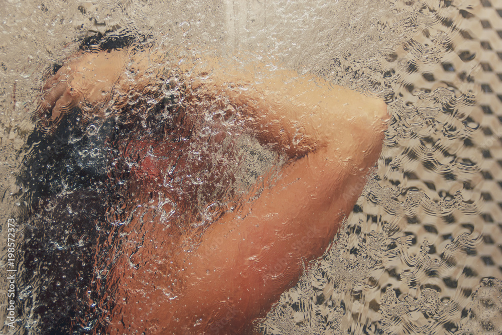 Beautiful woman in the shower behind glass with drops