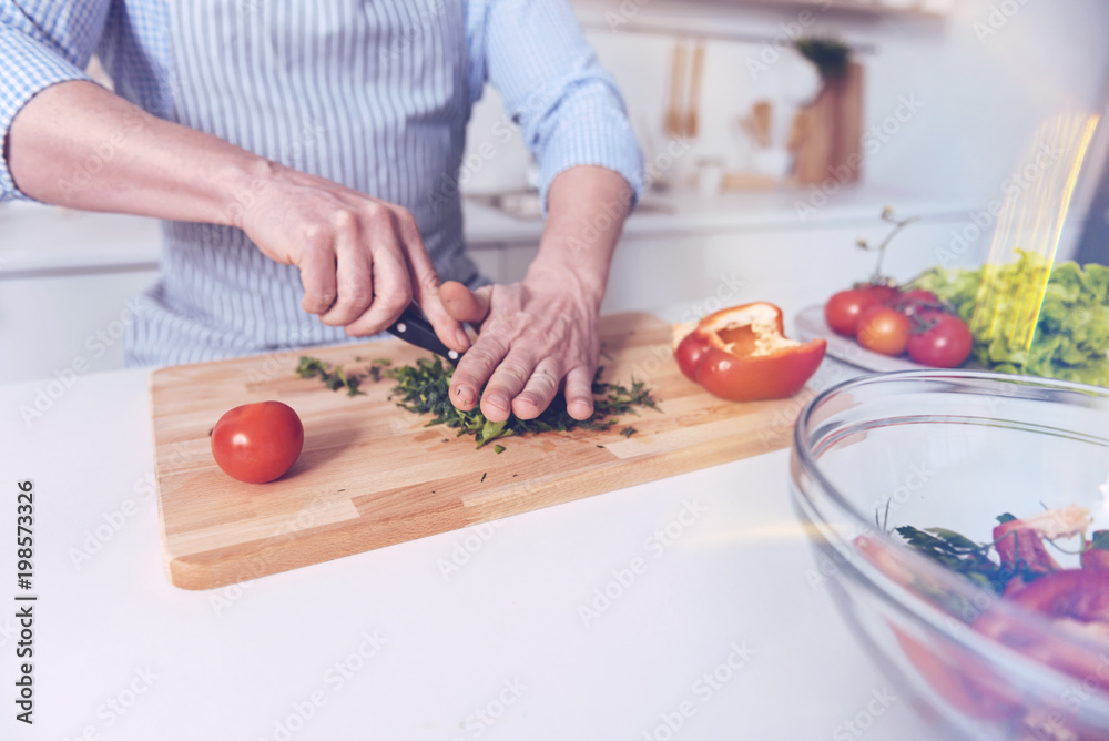Healthy nutrition. Pleasant man holding knife and cooking while cutting vegetables for salad