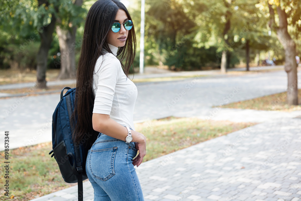 Hipster girl wearing khaki white sweat,t-shirt, jeans and back pack posing  walking in autumn city, minimalist urban clothing style.Stylish happy young  woman wearing boyfriend jeans and blue sunglasses Stock Photo | Adobe