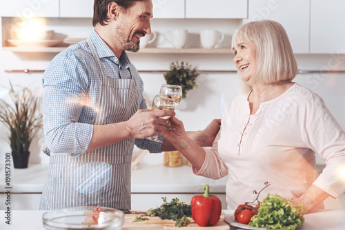 Happiness in the air. Positive aged woman standing in the kitchen with her adult son and drinking wine while resting together