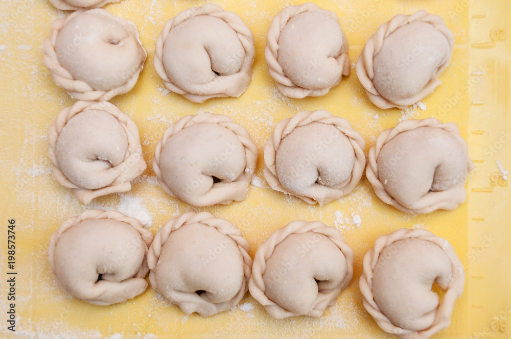 Raw dumplings lie in rows on a silicone yellow board top view Raw dumplings lie in rows on a silicone yellow board top view
