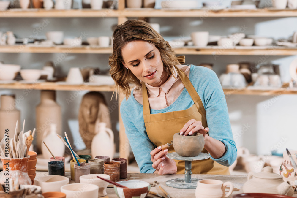 beautiful female potter decorating ceramic bowl in workshop