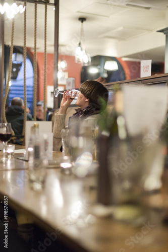 Single, alone, young adult woman drinks wine in pub