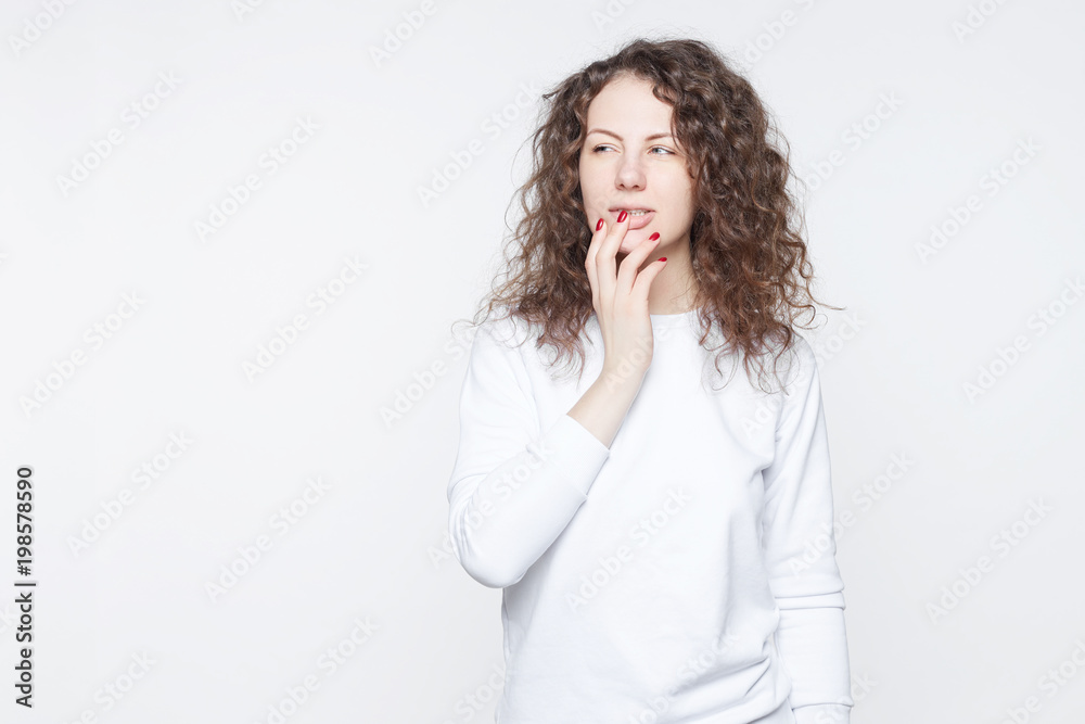 Young Caucasian attractive female with skeptic look, raises eyebrow in bewilderment, has some doubts and uncertainty, looks curiously aside, isolated over white background with copy space for text. Young Caucasian attractive female with skeptic look, raises eyebrow in bewilderment, has some doubts and uncertainty, looks curiously aside, isolated over white background with copy space for text.