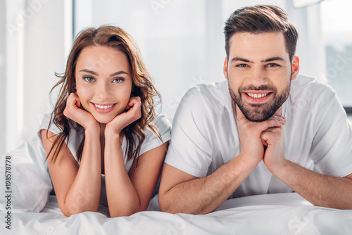 portrait of smiling couple looking at camera while resting on bed together