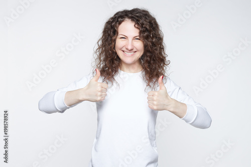 I like that. Good job. Happy young European female wearing casual long sleeved t-shirt making thumbs up sign and smiling cheerfully, showing her support and respect to someone. Body language concept.