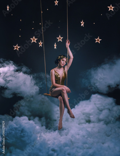 Fotografia An asterisk girl, swinging on a rocker in the clouds, among the stars and the night sky