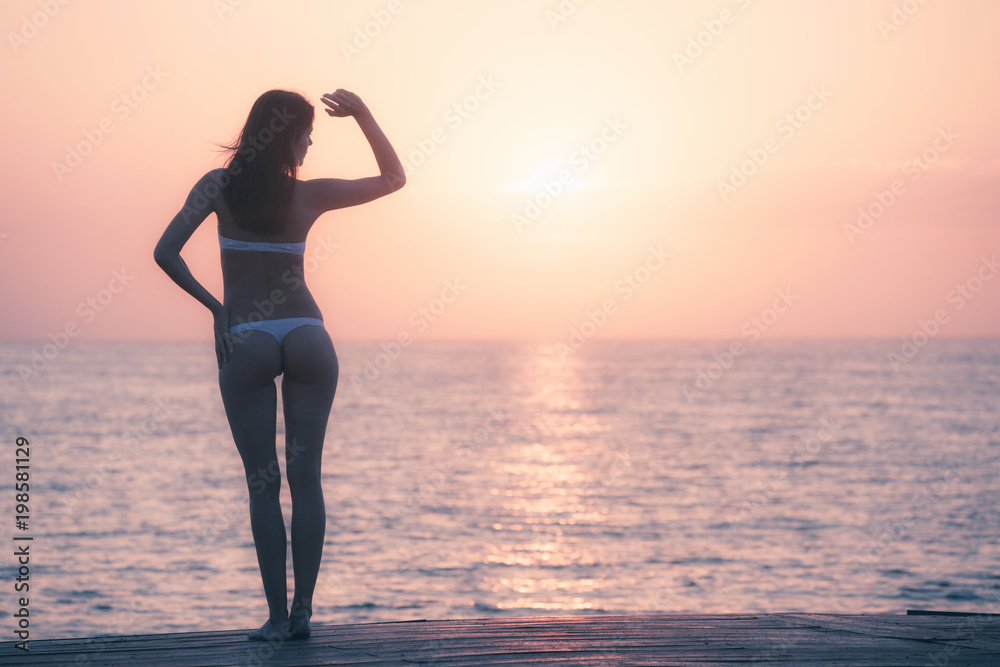 Silhouette of woman watching sunrise over ocean horizon