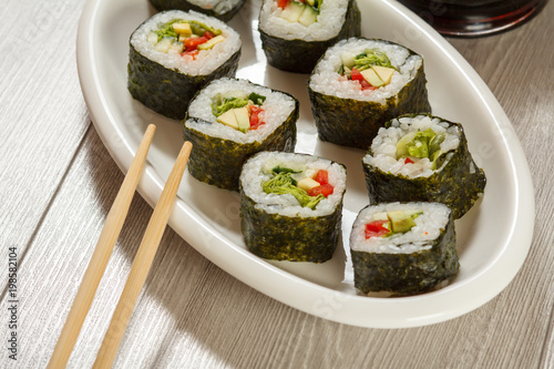 Sushi rolls with rice, pieces of avocado, cucumber and lettuce leaves on ceramic plate, chopsticks