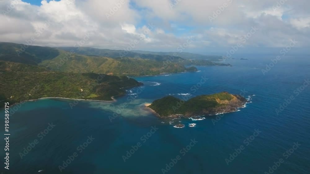 The coast of the tropical island with the mountains and the rainforest on a background of ocean with big waves.Aerial view: sea and the tropical island with rocks, beach and waves. Seascape: sky The coast of the tropical island with the mountains and the rainforest on a background of ocean with big waves.Aerial view: sea and the tropical island with rocks, beach and waves. Seascape: sky