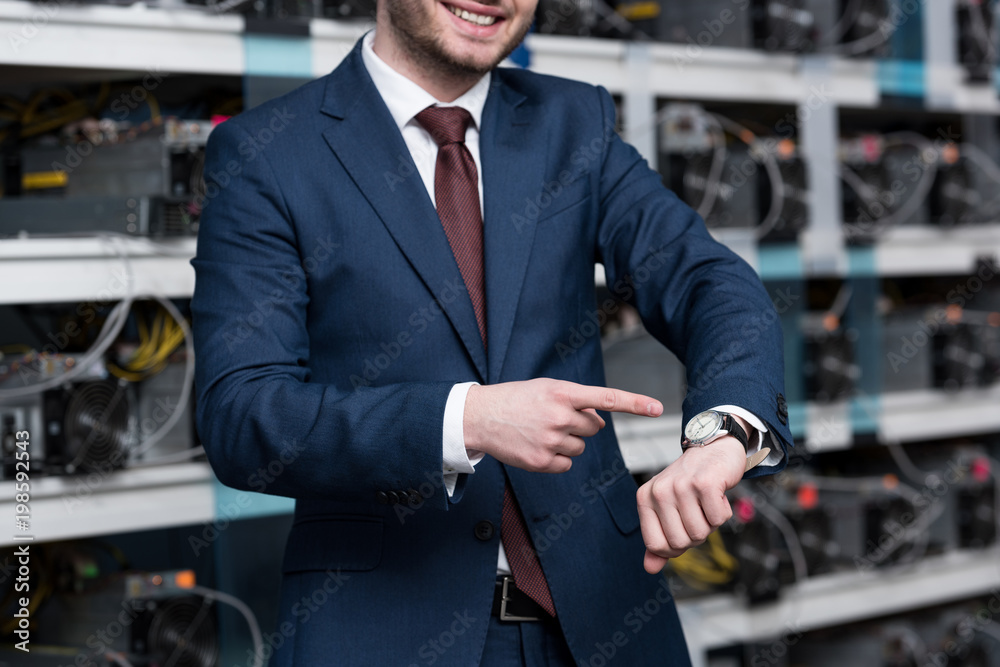 cropped shot of smiling businessman pointing at wristwatch at ethereum mining farm