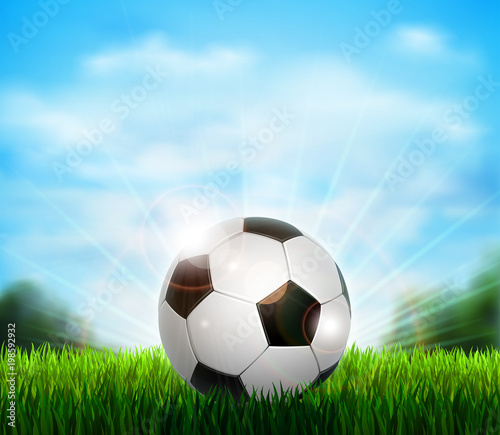 White and black soccer ball on the fresh green glade with grass. Background with blue sky  sunshine and sport equipment for playing football.
