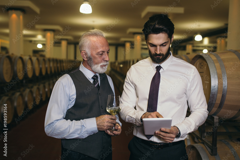 Winemakers in wine cellar holding glass of red wine and checking it. Sommeliers testing wines in winery. 