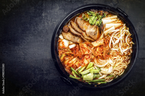 Traditional Korean kimchi jjigae with grilled pork belly and ramen as top view in a pot with copy space left