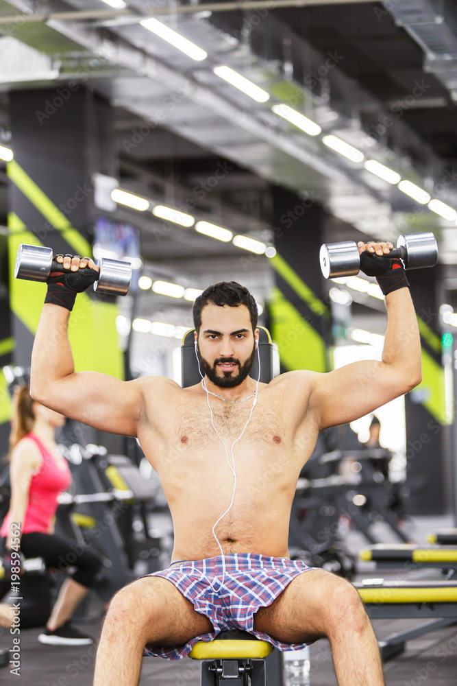 Topless bearded man holds metal dumbbells in the gym Topless bearded man holds metal dumbbells in the gym