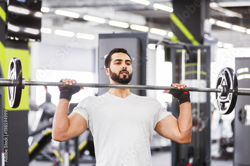 Bearded muscular man wears white t-shirt have workout with barbell in the gym