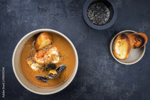 Traditional French fish soup with prawns and mussels as top view in a bowl