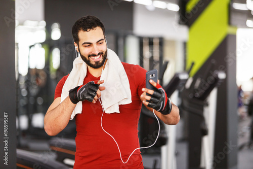 Bearded muscular smiling man using smartphone for videochat in the gym, hardworking rest photo