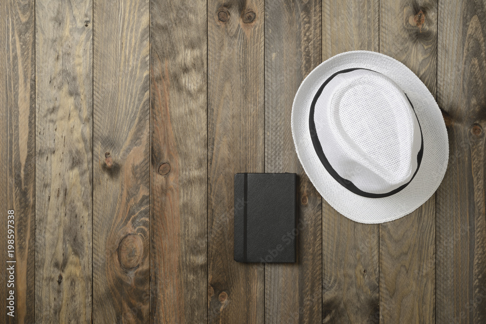 Sombrero blanco y libreta negra sobre fondo de madera