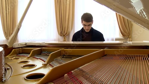 young pianist with glasses playing on a white grand piano photo