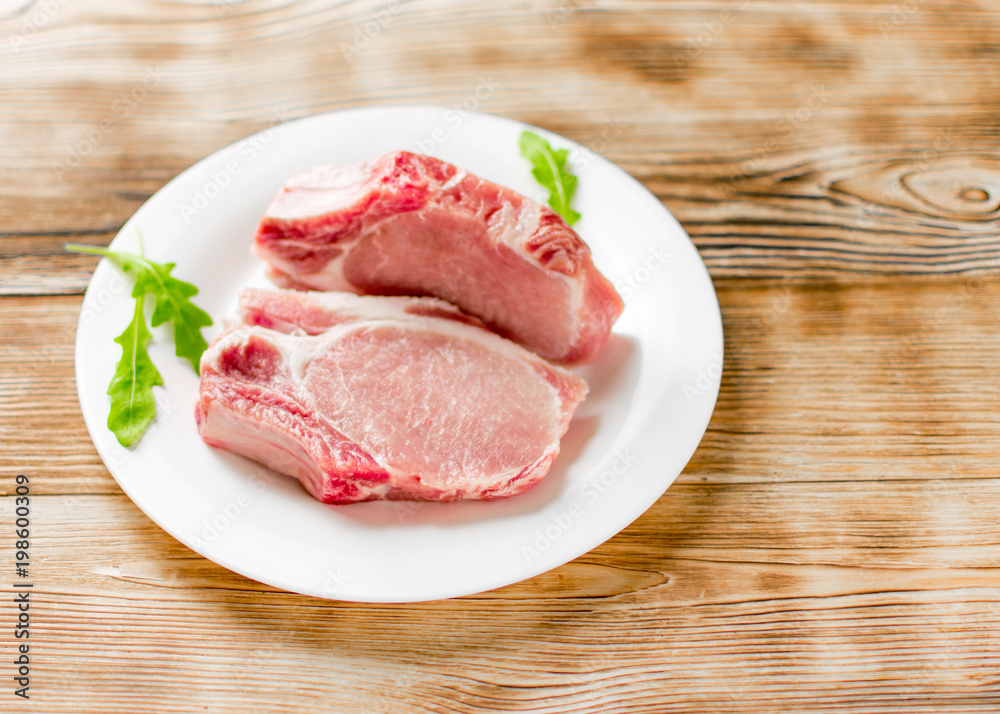 Raw pork brisket, ribs on a white plate on a wooden background. Raw pork brisket, ribs on a white plate on a wooden background.