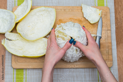 Girl cleans a pomelo on a wooden board photo