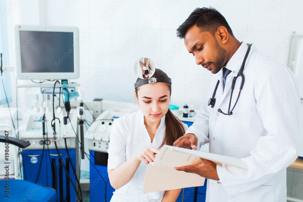 Asian ENT surgeon gives instruction for a mixed race of medical team using a tablet. Health in India Asian ENT surgeon gives instruction for a mixed race of medical team using a tablet. Health in India