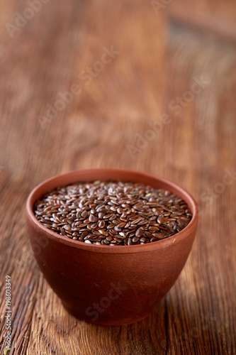 Flax seeds in ceramic bowl on rustic wooden background, top view, shallow depth of field