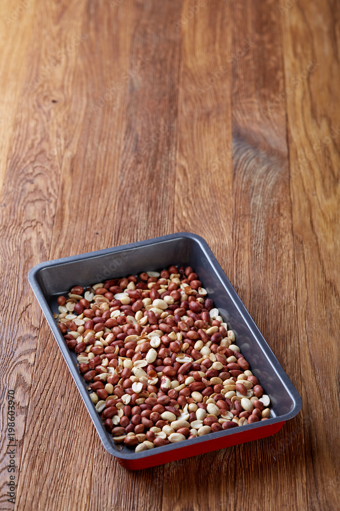 Mix of peeled raw peanut on baking tray over wooden background, selective focus, shallow depth of field. Mix of peeled raw peanut on baking tray over wooden background, selective focus, shallow depth of field.