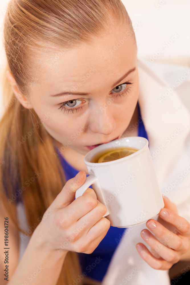 Woman lying on sofa under blanket drinking tea Woman lying on sofa under blanket drinking tea