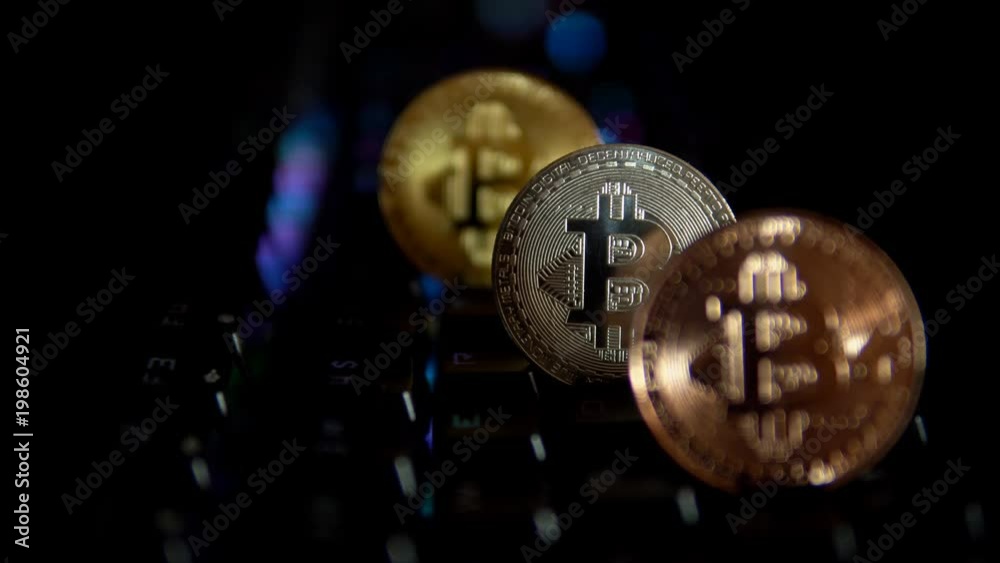 Gold, silver, bronze, coins bitcoin stand on a computer keyboard that flashes multicolored lights. This shoot is a seamless loop. Gold, silver, bronze, coins bitcoin stand on a computer keyboard that flashes multicolored lights. This shoot is a seamless loop.