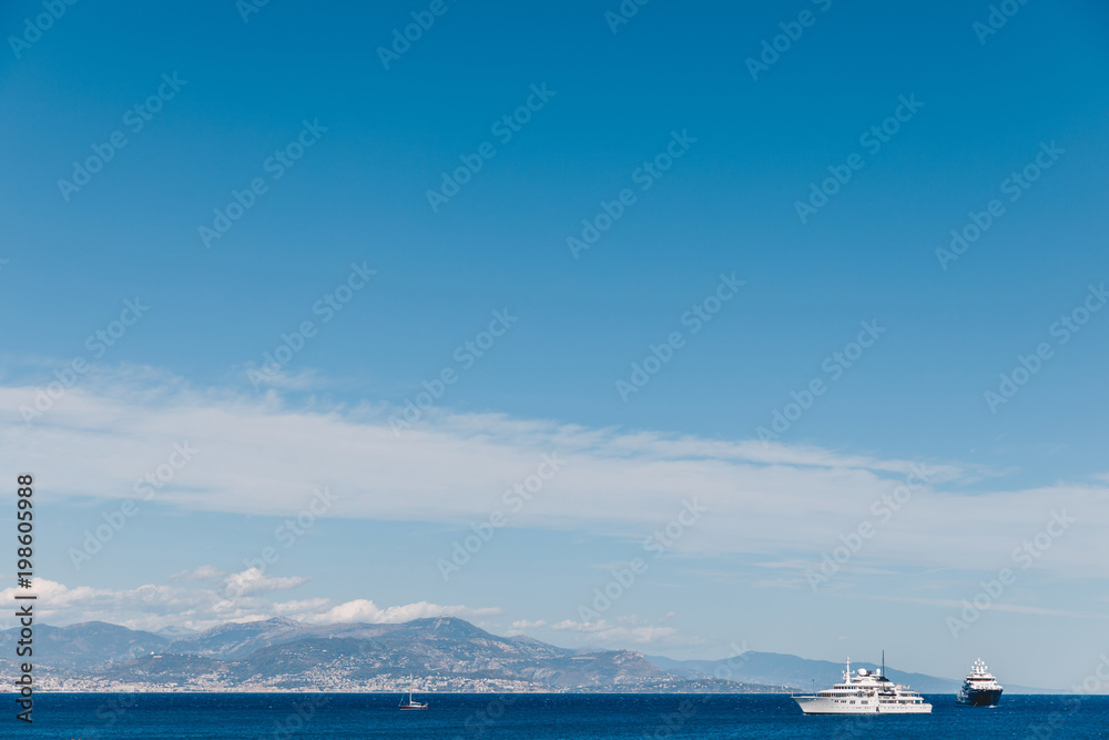 ships floating in sea on sunny day with mountains on background, Antibes, France