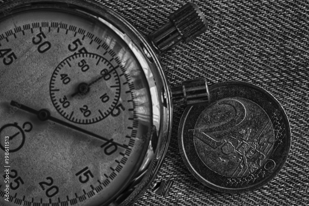Euro coin with a denomination of 2 euro and stopwatch on denim backdrop - business background. Euro coin with a denomination of 2 euro and stopwatch on denim backdrop - business background.