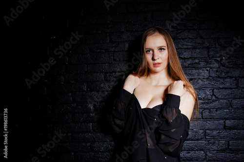 Studio shot of brunette girl in black blouse with bra and shorts against black brick wall. © AS Photo Family