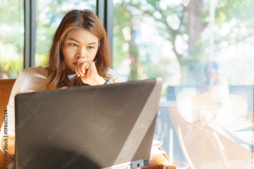 beautiful asian young business woman sitting near transparent window with laptop for her job and thinking about online marketing plan at cafe or coffee shop. business success concept. beautiful asian young business woman sitting near transparent window with laptop for her job and thinking about online marketing plan at cafe or coffee shop. business success concept.
