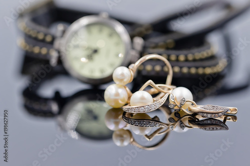 Gold earrings with pearl on the background of watches